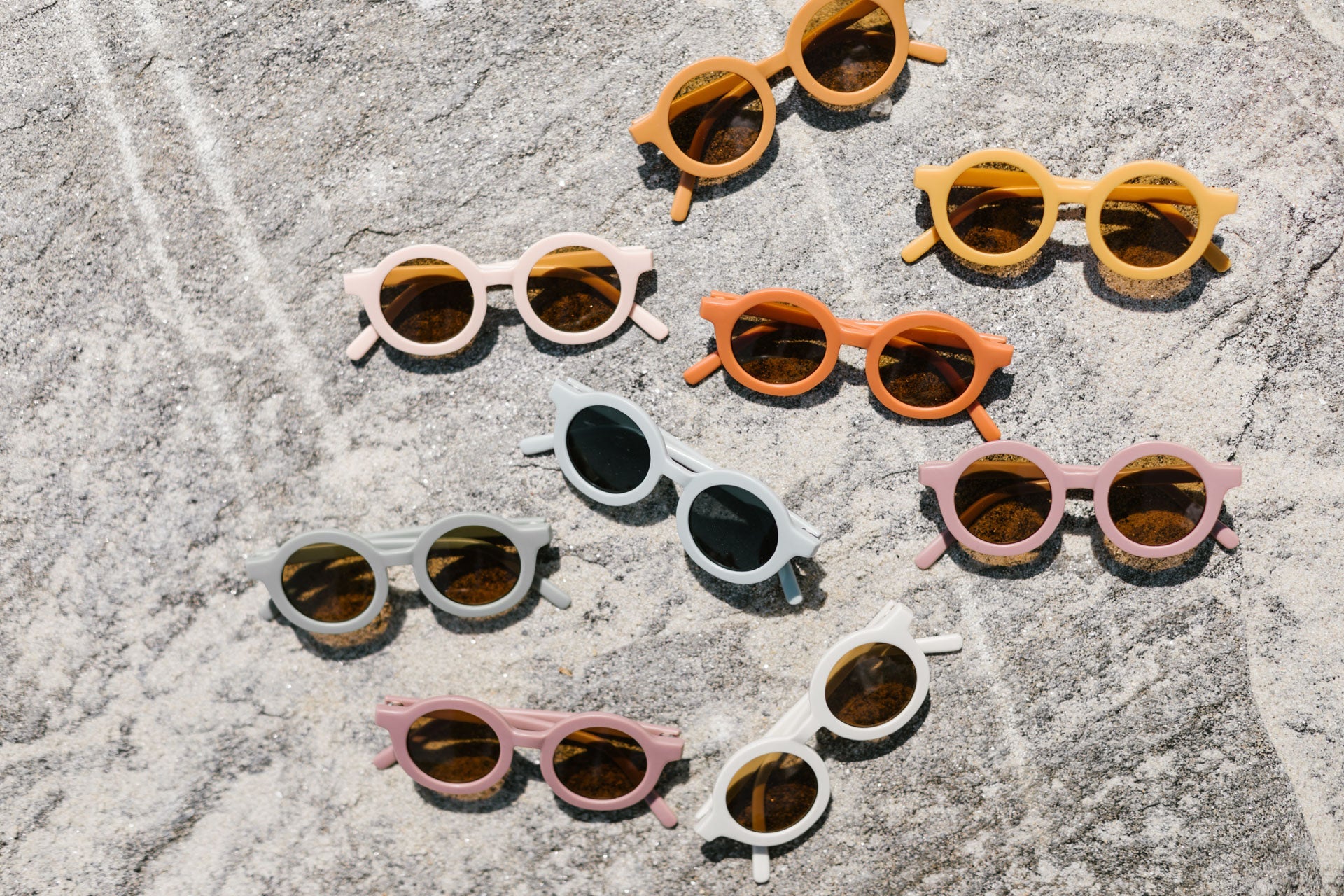 A collection of colorful round sunglasses arranged on a textured stone surface.