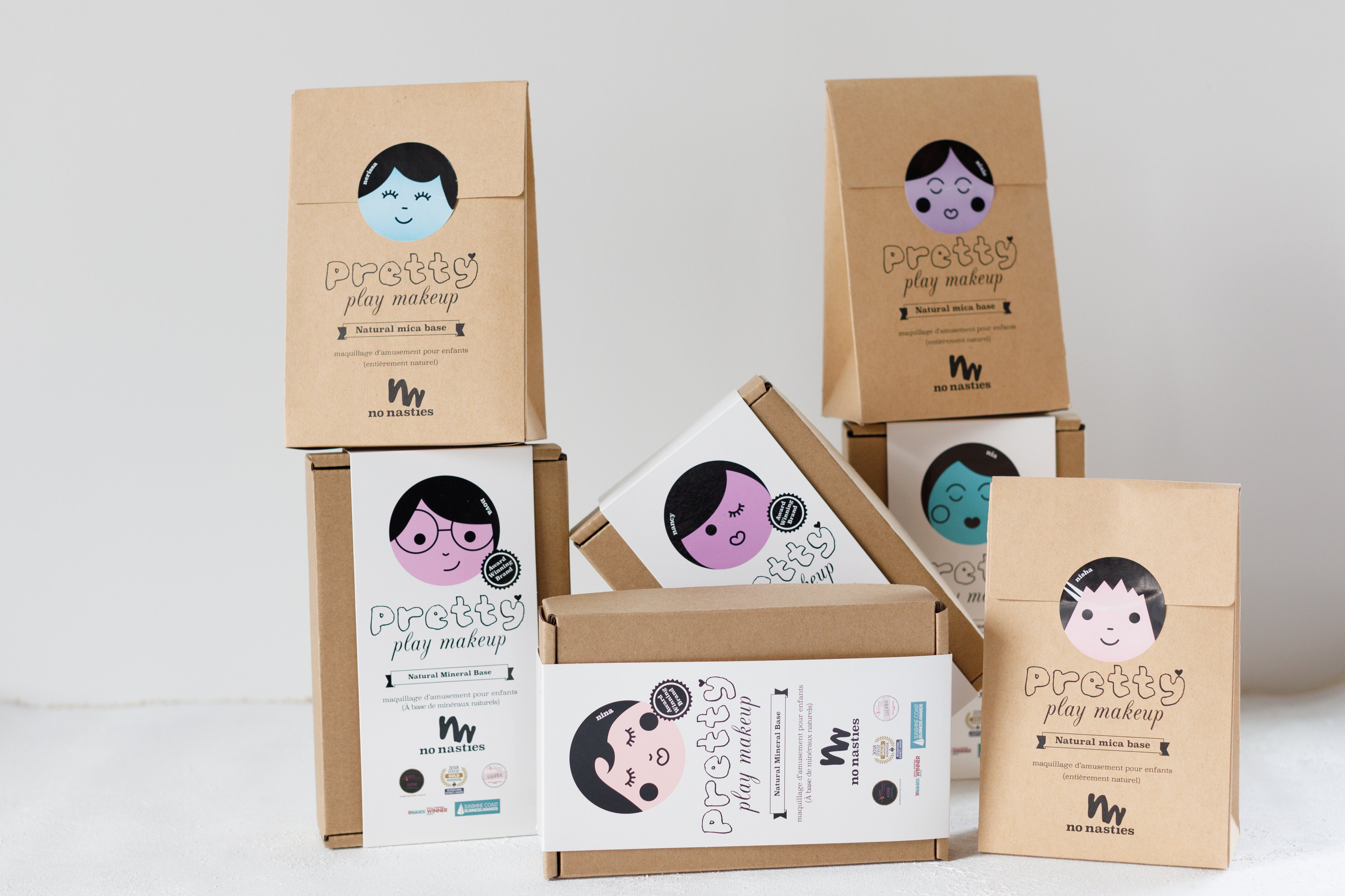 Boxes of Pretty Play Makeup, a natural makeup brand for kids, are displayed. The packaging features illustrated faces with different expressions and colors.