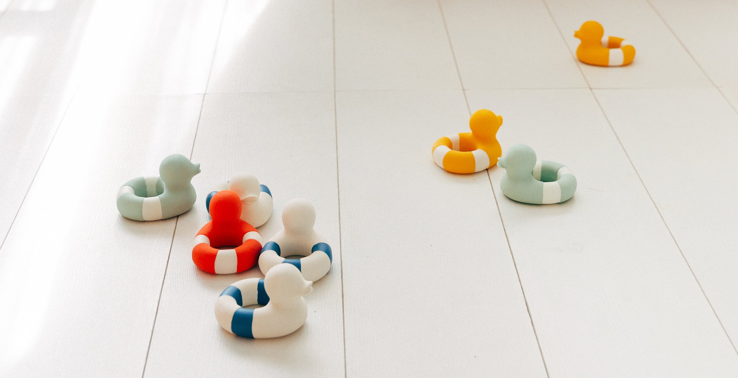 Several toy ducks in various colors, each with rings, are scattered on a white floor.