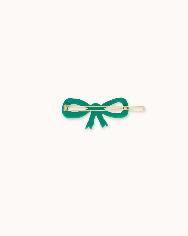 A "bow big clip in emerald" by tiny cottons, featuring an elegant gold pin, rests on a white background, seamlessly merging style with functionality.