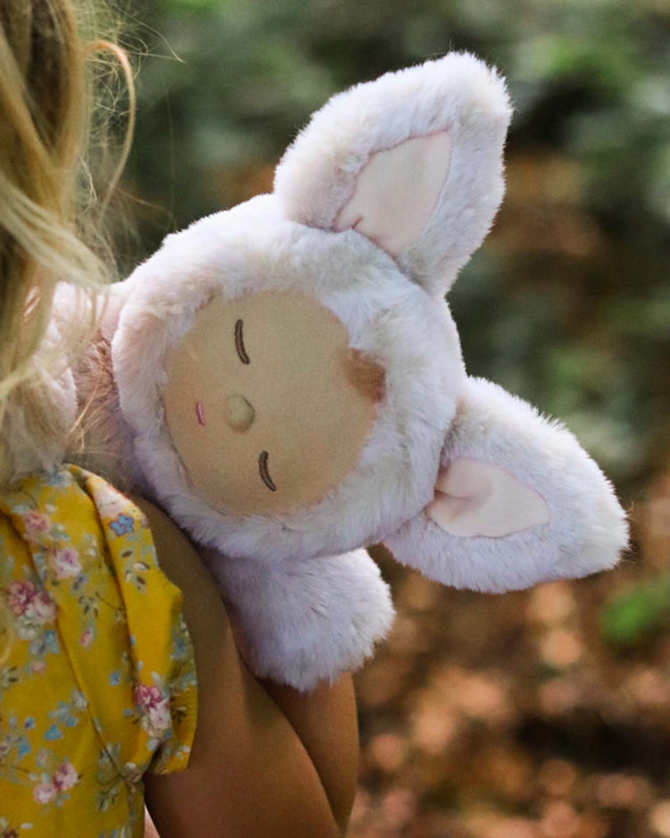 A child in a yellow floral dress cuddles an Olli Ella Cozy Dinkum Fox Fenix plush toy with large ears.