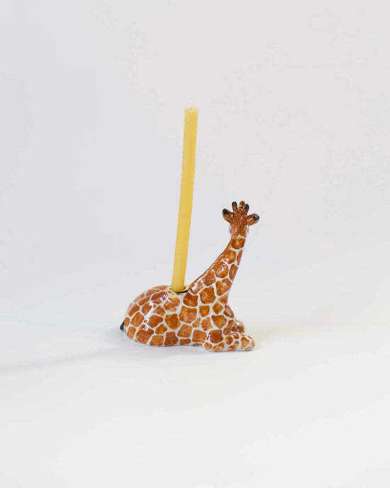 A decorative hand-painted giraffe-shaped ceramic candle holder with a yellow candle, set against a plain white background.