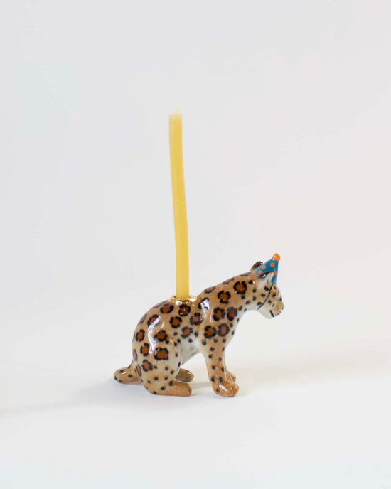 A hand-painted, ceramic jaguar-shaped candle holder with a yellow candle inserted on its back, positioned against a plain white background. (Brand: camp hollow)