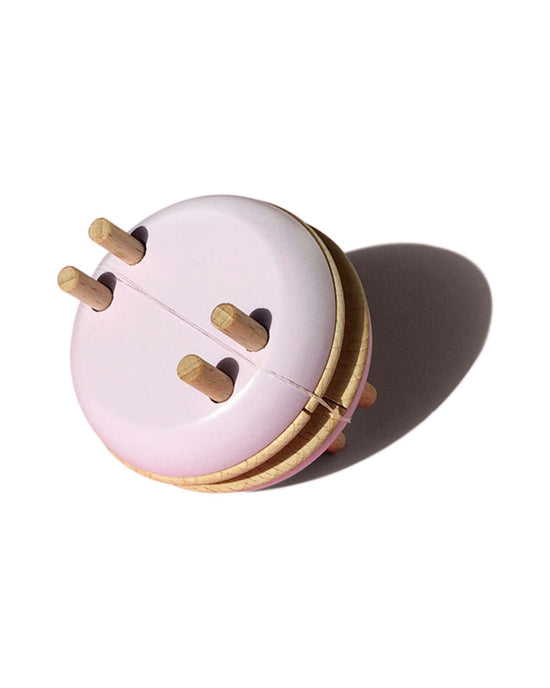 Pink macaron pom maker with four holes, perfect for DIY decorations, casting a shadow on a white surface.